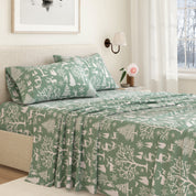 Green and white patterned bedspread on a bed in a bedroom with a lamp and window in the background.